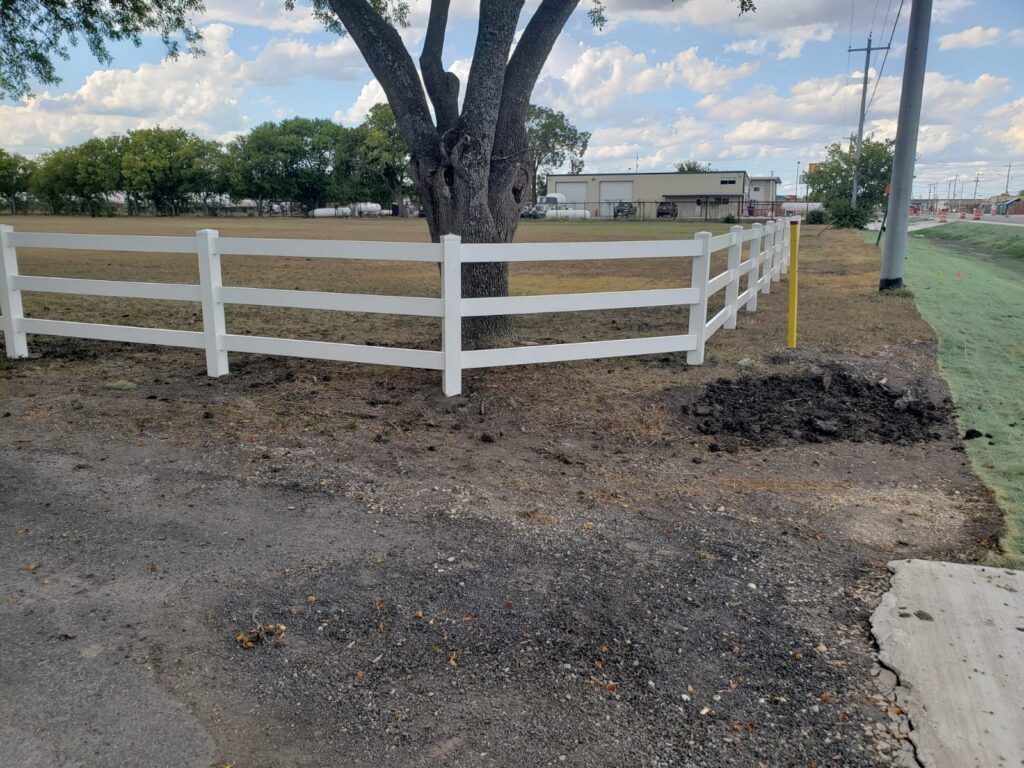 White vinyl fence across a field under a big tree